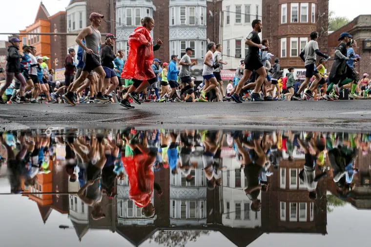Runners are reflected in a puddle after it rained at Broad Street and Windrim Avenue during the 44th annual Independence Blue Cross Broad Street Run in Philadelphia, Pa on Sunday, April 30, 2023.