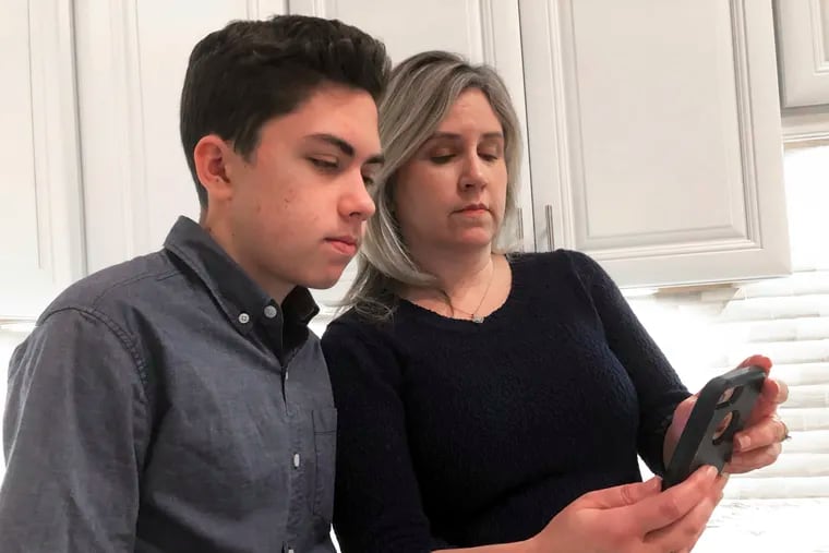 Grant Thompson and his mother, Michele, look at an iPhone in the family's kitchen in Tucson, Ariz., on Thursday, Jan. 31, 2019. The 14-year-old stumbled upon a bug in the iPhone's FaceTime group-chatting feature on Jan. 19 while calling his friends to play a video game. With the bug, a FaceTime group-chat user calling another iPhone, iPad or Mac computer could hear audio, even if the receiver did not accept the call. (AP Photo/Brian Skoloff)