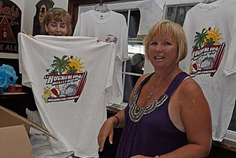 Washington Twp. volunteers Eleanor Bollendorf (right) and Kathy Quattrochi set up T-shirts for sale at the Fifth Quarter Club’s summer benefit for high school sports. (AKIRA SUWA / Staff Photographer)
