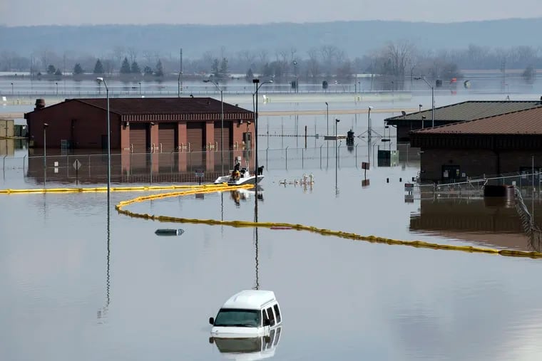 In this March 18, 2019 photo released by the U.S. Air Force, environmental restoration employees deploy a containment boom from a boat on Offutt Air Force Base in Neb., as a precautionary measure for possible fuel leaks in the flooded area. Surging unexpectedly strong and up to 7 feet high, the Missouri River floodwaters that poured on to much the Nebraska air base that houses the U.S. Strategic Command overwhelmed the frantic sandbagging by troops and their scramble to save sensitive equipment, munitions and aircraft.