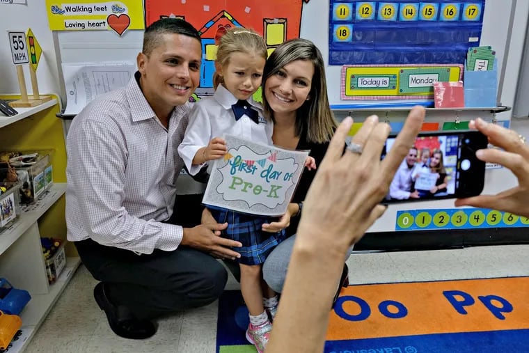 Parents Noel, 34, left, and Gaby Socorro, right, both CPAs, pose for a picture with their daughter Mila, taken by her teacher Kelly Barge, as Pre-K students attended their first day of school at iPrep Academy near downtown Miami, Fla.