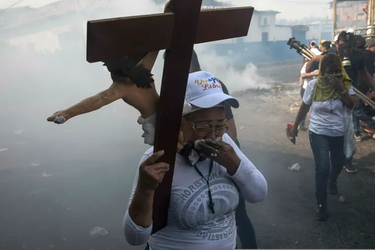 A woman carries a cross during clashes between the opposition and the Bolivarian National Guard in Urena, Venezuela, near the border with Colombia, Saturday, Feb. 23, 2019. Venezuela's National Guard fired tear gas on residents clearing a barricaded border bridge between Venezuela and Colombia on Saturday, heightening tensions over blocked humanitarian aid that opposition leader Juan Guaido has vowed to bring into the country over objections from President Nicolas Maduro.