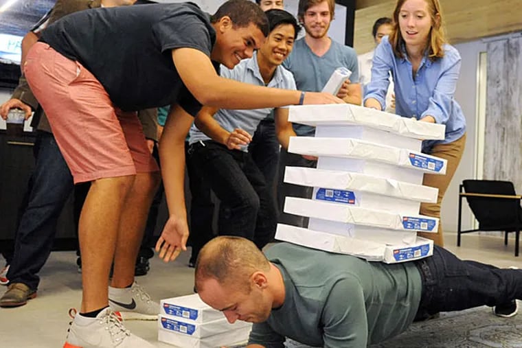 #StackThatPaper: Zach Robbins, 28, CEO of Leadnomics, planks while employees stack paper on his back. (CLEM MURRAY / Staff)