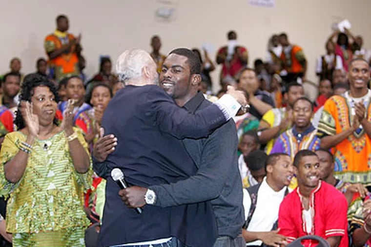 Eagles quarterback Michael Vick, right, is hugged by Bilal Qayyum of the Father's Day Rally Committee, after Qayyum introduced him to the Imhotep Charter students. Christine Wiggins, CEO and Founder of Imhotep is left. (Charles Fox / Staff Photographer)