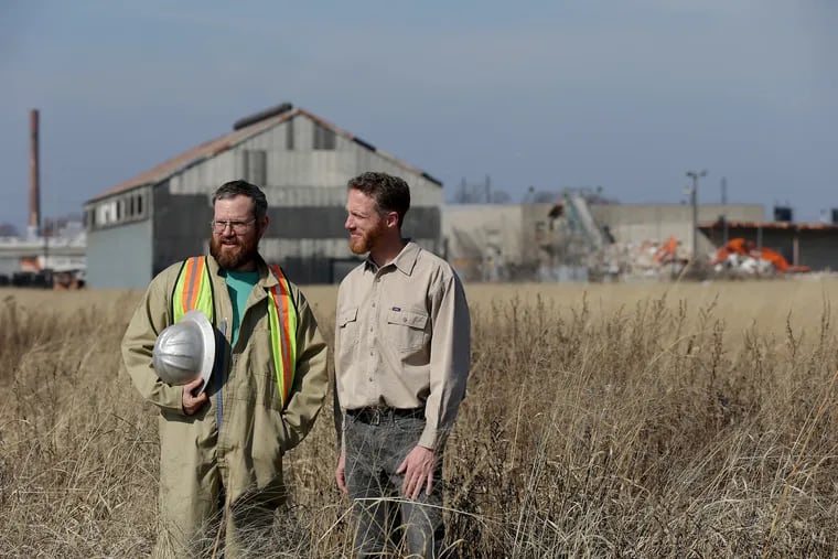 Billy Dufala, left, co-founder of RAIR (Recycled Artist In Residency), and John Wybar, right, owner of Revolution Recovery, stand on the Metal Bank Superfund Site in February 2018.  Federal and state agencies have reached an agreement for utility companies that polluted the properties as far back as the 1970s to pay nearly $1 million Revolution Recovery did not cause the pollution, though it now owns the site.