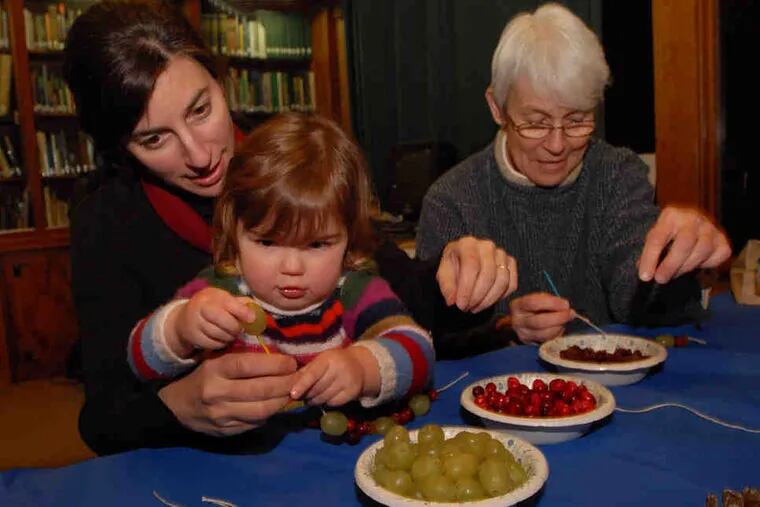 At an edible-ornament workshop at Bowman's Hill Wildlife Preserve, Ani Orphanides helps daughter Luca Wilson, 2, string cranberries while her mother, Barbara Orphanides, works on her own decorations. One key is knowing what attracts birds but keeps pests away.