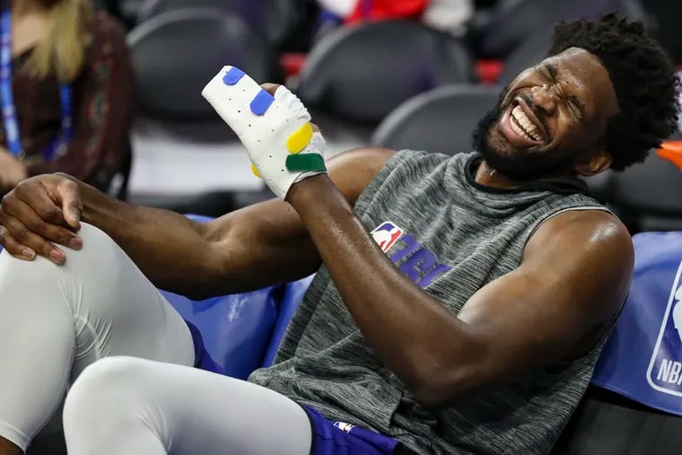 Joel Embiid laughs on the bench wearing a wrap on his left hand before the start of a game against the Brooklyn Nets at the Wells Fargo Center in Philadelphia on Wednesday. Embiid is out with a torn radial collateral ligament in the ring finger of his left hand. He had surgery on his hand last Friday afternoon in New York.