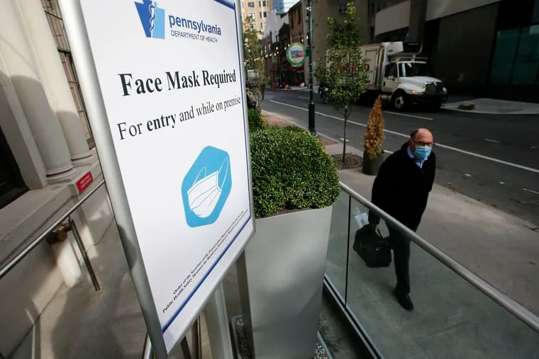 A pedestrian walks near a Pennsylvania Department of Health Face Mask Required sign posted at the Warwick Hotel Rittenhouse Square in Center City on Thursday, November 19, 2020.
