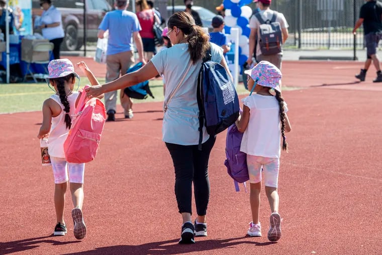 Yasaret Beltran (center) with six-year-old twin daughters, Lilliana (left) and Mia, walking away with new backpacks during Philly's back-to-school tour on Aug. 10 outside South Philadelphia High School.
