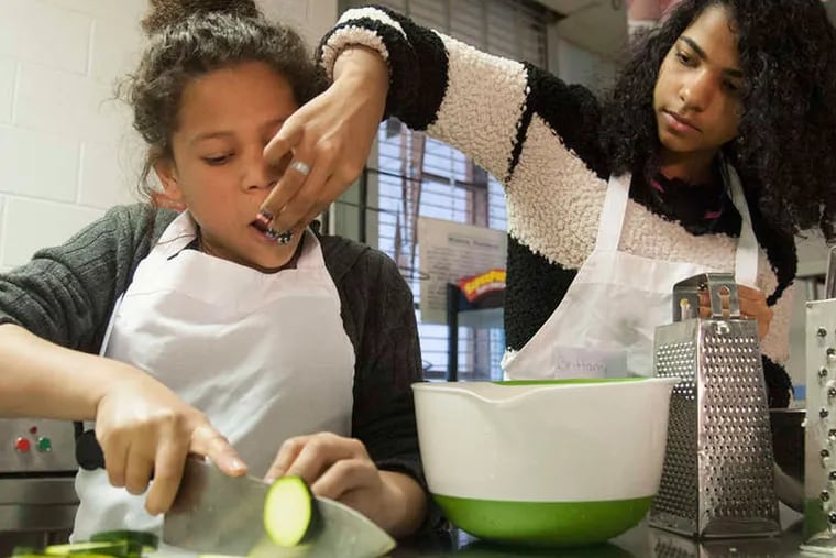 Tatiana Castillo gets a taste of cheese from classmate Brittany Jones while cutting vegetables for a quiche that will be made at Roberto Clemente Middle School.