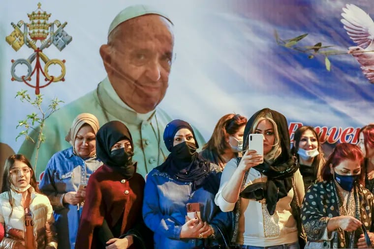 Women wait outside the Chaldean Cathedral of Saint Joseph, in Baghdad, Iraq, Saturday, March 6, 2021, where Pope Francis, depicted on a giant poster at their back, is concelebrating a mass. Earlier today Francis met privately with the country's revered Shiite leader, Grand Ayatollah Ali al-Sistani.