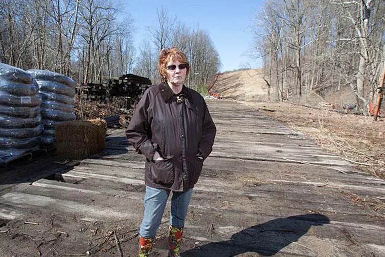 Lynda Farrell in her yard in Downingtown, where Williams Transco is building a pipeline. Farrell is standing on a road constructed of wooden ties, surrounded by construction material. (ED HILLE / Staff Photographer)