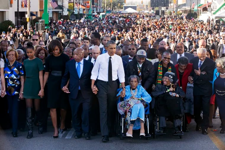 In this March 7, 2015, photo, President Barack Obama (center) walks as he holds hands with Amelia Boynton Robinson, who was beaten during "Bloody Sunday," as the first family and others, including Rep. John Lewis (D., Ga.), left of Obama, walk across the Edmund Pettus Bridge in Selma, Ala., for the 50th anniversary of "Bloody Sunday," a landmark event of the civil rights movement. From left are Marian Robinson, Sasha Obama, first lady Michelle Obama, President Obama, Boynton Robinson, and Adelaide Sanford, also in a wheelchair.