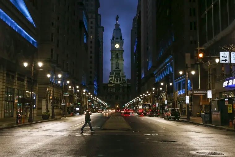 A lone soul crosses the street at Broad and Locust Streets at dusk on Monday, the day a stay-at-home order went into effect for city residents and was announced for the surrounding counties.