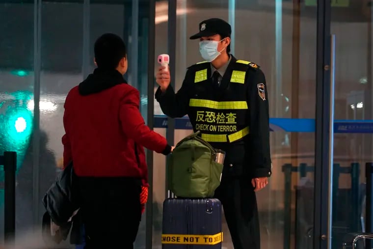 An airport staff member uses a temperature gun to check people leaving Wuhan Tianhe International Airport in Wuhan, China, Tuesday, Jan. 21, 2020. Heightened precautions were being taken in China and elsewhere Tuesday as governments strove to control the outbreak of a novel coronavirus that threatens to grow during the Lunar New Year travel rush.
