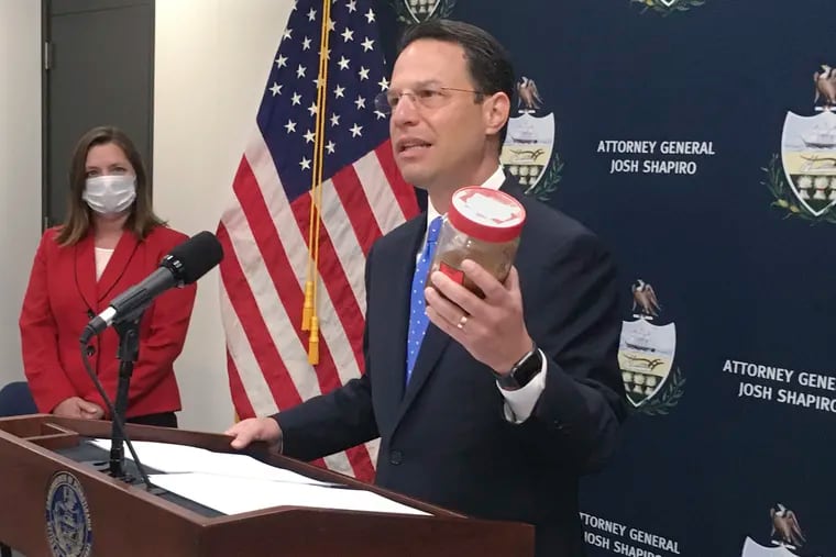 Pennsylvania Attorney General Josh Shapiro, right, holds a jar of discolored tap water during a news conference. He said the sample was from the home of a state resident whose well had been tainted by nearby natural gas drilling.