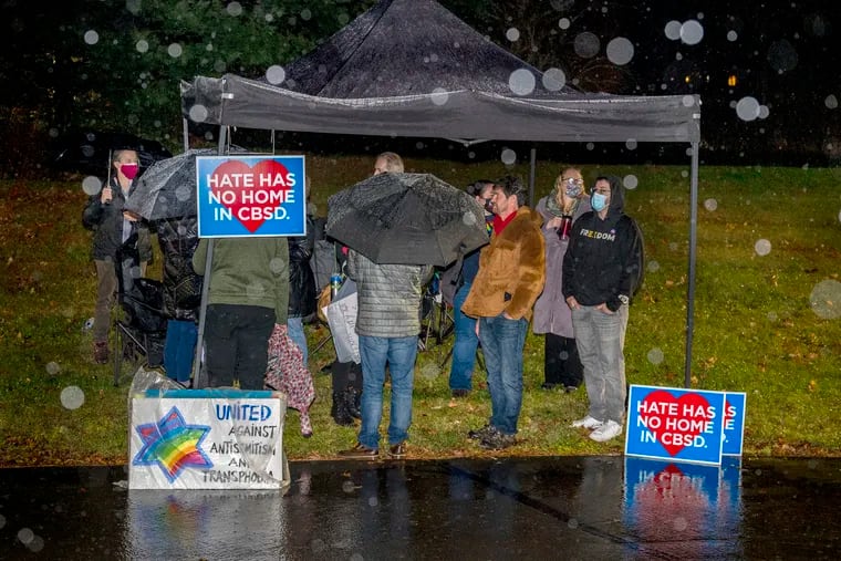 Community members wait in the rain with their signs outside the Central Bucks School Board meeting on Dec. 6. The district announced schools would be closed Monday due to an unprecedented number of teacher absences because of a surge in COVID-19 cases.