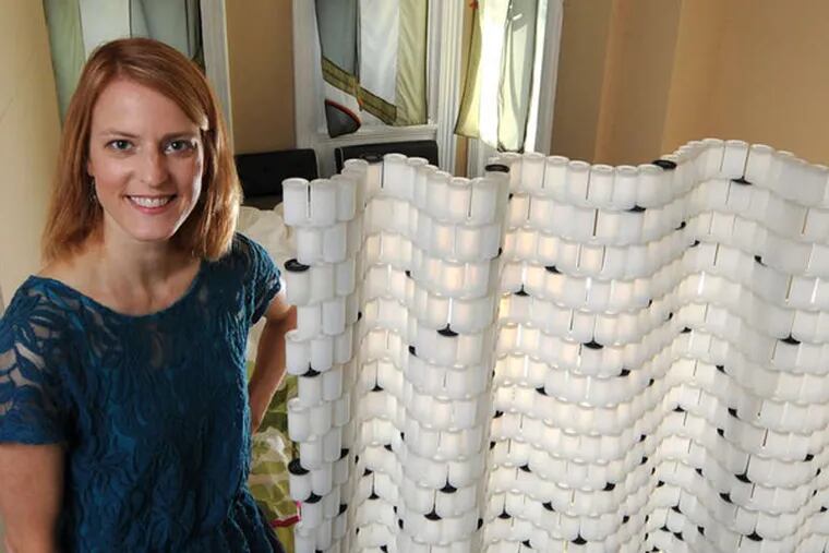Tiffany Threadgould with a room divider made from hundreds of old 35mm film canisters.