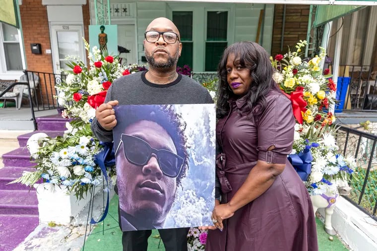 Thomas Blackwell VI and his wife, Sajda, pose for a portrait in front of their West Philadelphia home last month holding a photo of Charles Edward Blackwell II.