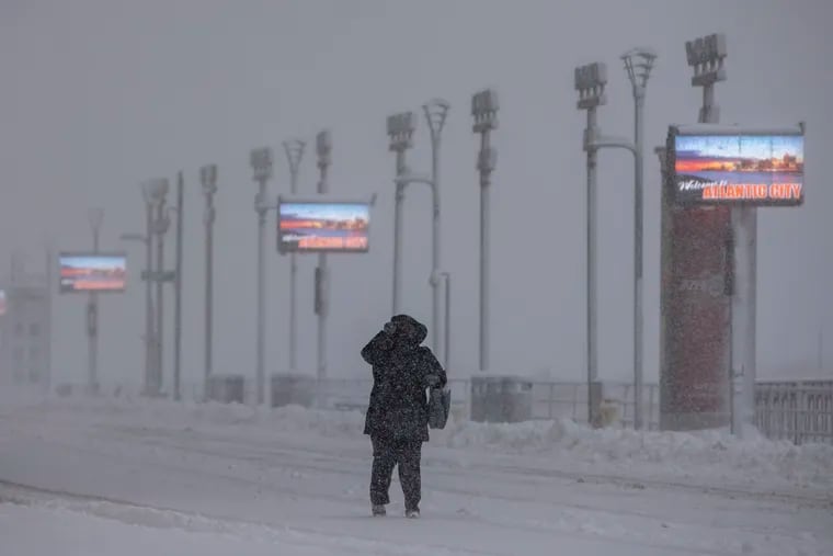 A pedestrian on boardwalk tries to cover her face from snow and wind on a cold snowy morning in Atlantic City.