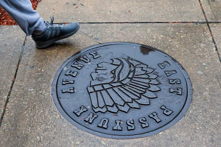 A pedestrian walks near a the Native American manhole cover logo on the 1700 block of East Passyunk Avenue.