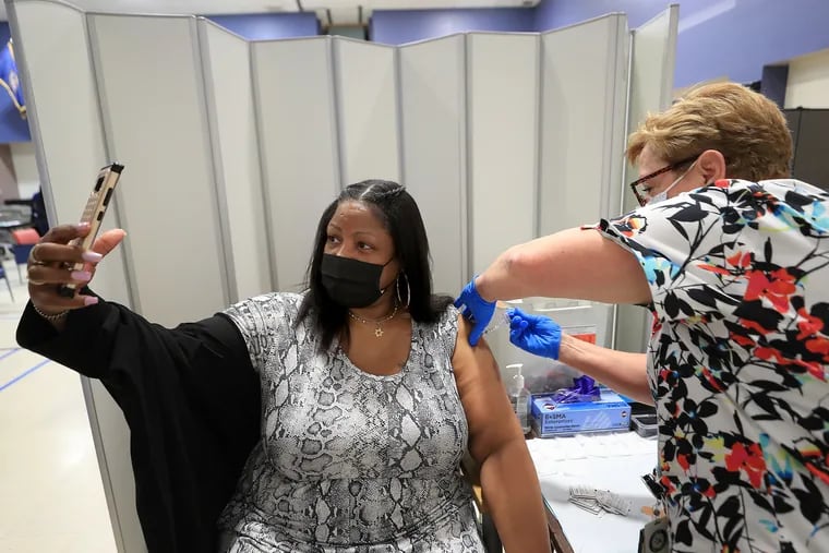 Kena Marshall-Owens (left), who is the wife of a veteran, records the moment as LPN Penny Roche-Walls gives her a COVID-19 vaccine at the vaccine clinic at the Veterans Affairs hospital in Philadelphia in May.