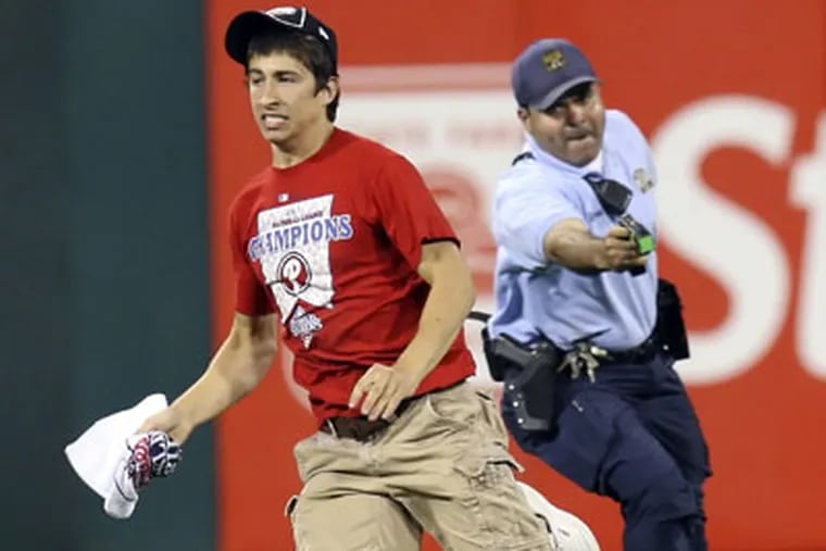 A Philadelphia police officer with Taser in hand chases a Phillies' fan who ran on the field during Monday night's game. (Steven M. Falk / Staff Photographer)