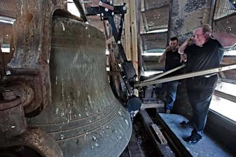 In the clock tower of St. John the Baptist Church in Manayunk, the Rev. James A. Lyons (right) and maintenance worker John Woods react as the bell chimes 3 p.m. A neighbor complained to the city about the 7 a.m. peal. (DAVID M WARREN / Staff Photographer)