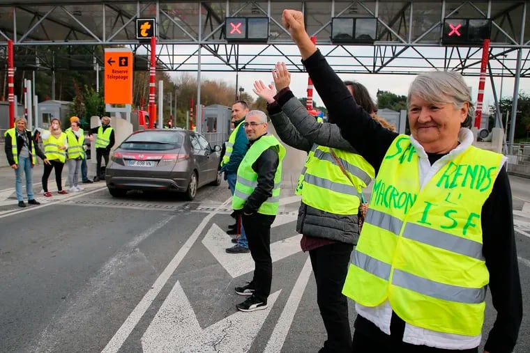 A demonstrator wearing a yellow jacket reading " Macron give us the wealth tax" protests at the toll gates on a motorway at Biarritz southwestern France, Wednesday, Dec.5, 2018.The concessions made by French president Emmanuel Macron's government in a bid to stop the huge and violent anti-government demonstrations seemed on Wednesday to have failed to convince protesters, with trade unions and disgruntled farmers now threatening to join the fray.(AP Photo/Bob Edme)