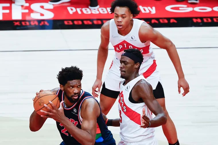 Sixers center Joel Embiid holds the basketball against Toronto Raptors forward Pascal Siakam and forward Scottie Barnes during game six of the first-round Eastern Conference playoffs on  April 28 in Toronto.