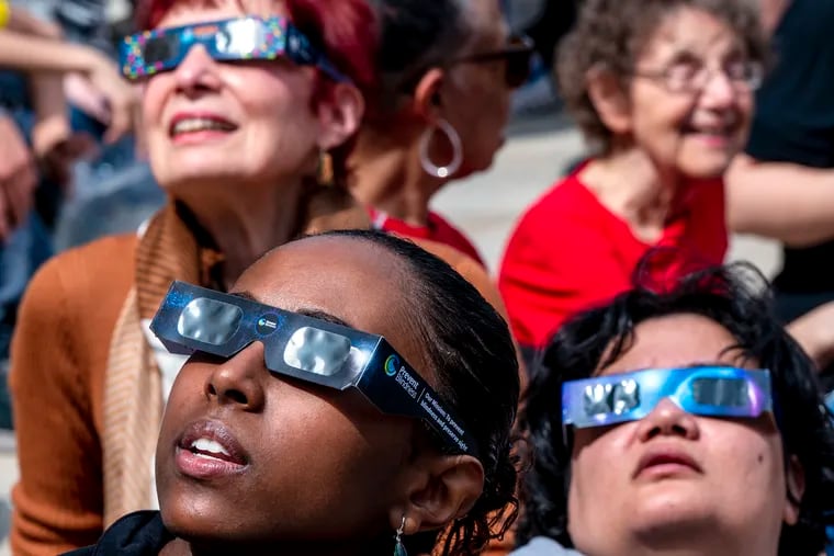 Wearing special glasses Addis Getnet (front, left), 19, of Lansdowne, and others watch the partial eclipse during a free community-wide eclipse viewing party at the Franklin Institute.