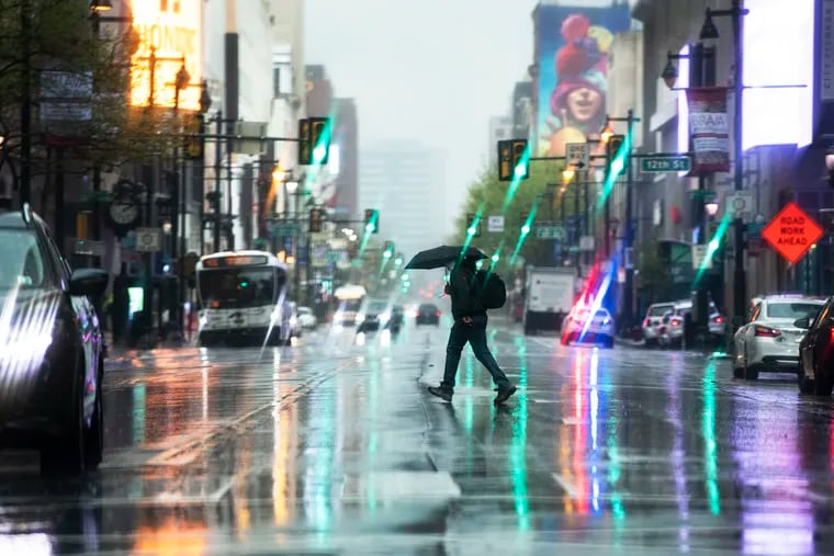A pedestrian shields from the rain with an umbrella as crosses 13th and Market Street during a storm last month.