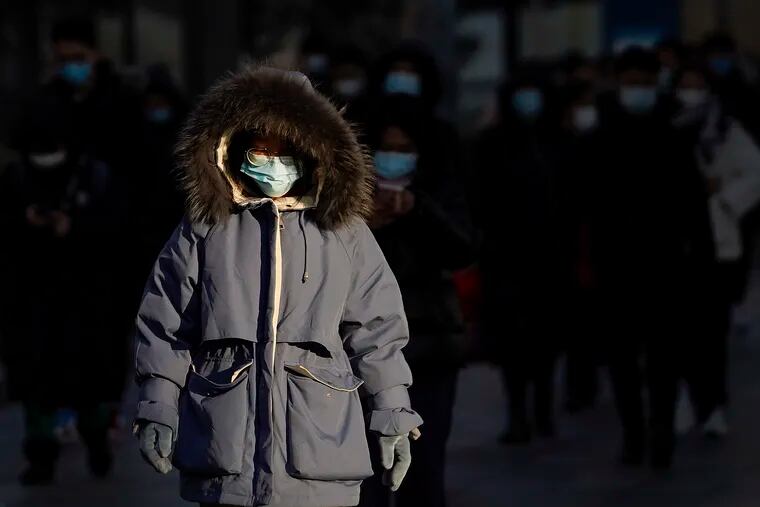 A woman wearing face masks to help curb the spread of the coronavirus heads for work during the morning rush hour in Beijing, Monday, Jan. 4, 2021.