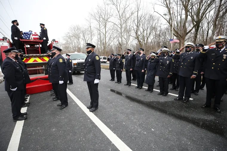 Members of the Philadelphia Fire Department salute as the casket of fellow firefighter John Evans is placed on top of a fire truck on Feb. 23, 2021. Evans, a 37-year veteran of the Philadelphia Fire Department, died in the line of duty on Feb. 12 after a battle with COVID-19.