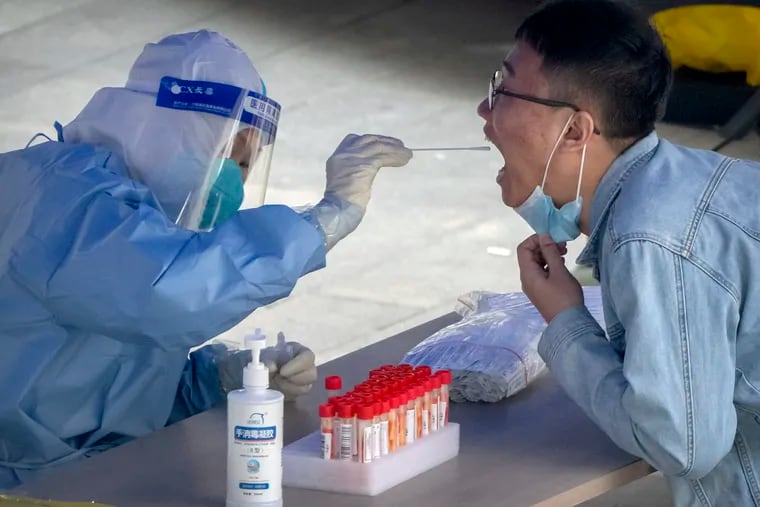 A worker in a protective suit swabs a man's throat for a COVID-19 test at a site in an office complex in Beijing.