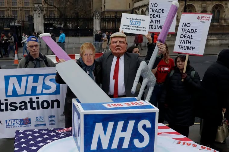 A coalition of NHS (National Health Service) campaigners led by "Keep Our NHS Public" and "We Own It", pose for photographs with masks of U.S. President Donald Trump, right, and British Prime Minister Boris Johnson carving up the NHS with a giant knife and fork, as they take part in a demonstration on Parliament Square, backdropped by the Houses of Parliament in London, Monday, Nov. 25, 2019.