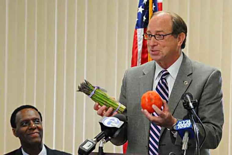 NJ Sec. of Agriculture Doug Fisher (light suit) holds a bunch of asparagus and a tomato during a press conference May 8, 2013 in Mickel Towers in Camden where the Camden Children's Garden announced its Mobile Market initiatiive, which aims to bring fresh produce to Camden neighborhoods via trucks and trailers.  At left is State Assemblyman Gilbert "Whip" Wilson who sponsored legislation enabling this initiative.  ( CLEM MURRAY / Staff Photographer )