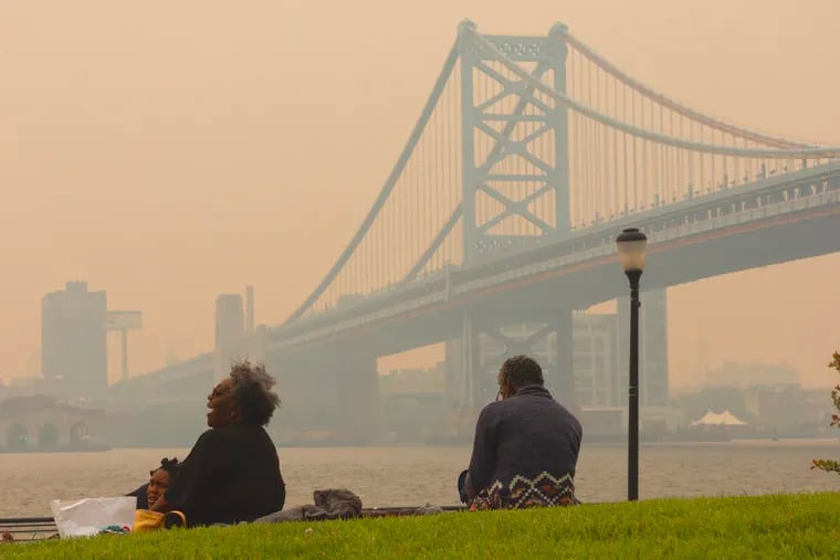 The Jackson Family from Pennsauken sits along the Camden waterfront with Philadelphia and the Ben Franklin Bridge in a smoky haze in the background on Wednesday.