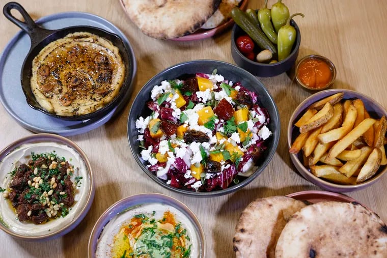 A spread of food at the new Dizengoff, including pita; pickles and olives; Turkish hummus with brown butter, crispy garlic, urfa pepper; roasted squash with Bulgarian feta, dates, radicchio, and pepitas; fries with tehina ketchup; hummus Yerushalmi with beef, baharat, pine nuts, and parsley; and hummus with green tehina.