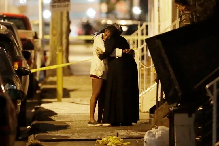 As night falls, two people embrace across the street from 3344 N. Water St. in the Kensington section of Philadelphia on Sunday. Earlier in the afternoon an unidentified person shot into a home there killing a 2-year-old girl and wounding two others.