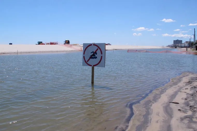 A July 31 photo shows a no-swimming sign in one of numerous large pools of water that have formed on the beach in Margate.