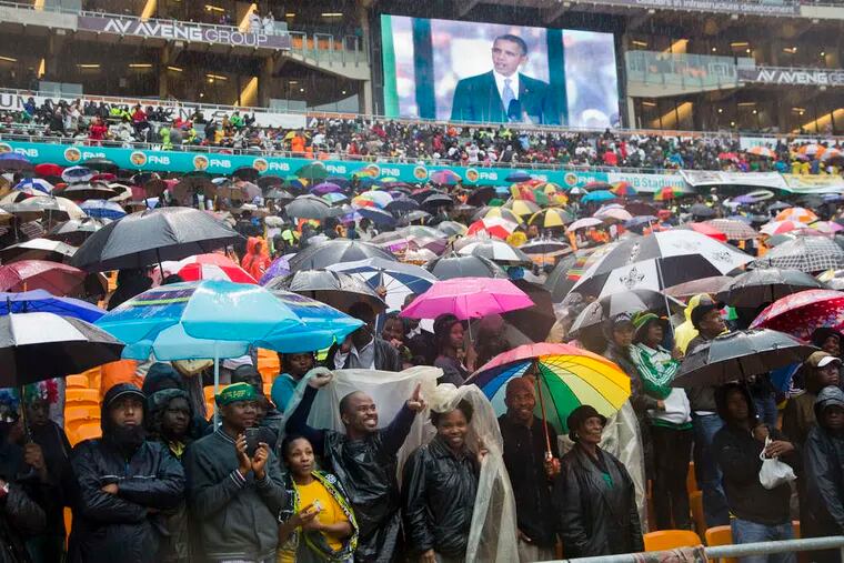 Spectators cheer amid an ocean of umbrellas as President Obama, shown on a big screen, speaks at the service. The rain was seen as a blessing by many. &quot;Only great, great people are memorialized with it,&quot; said a South African.