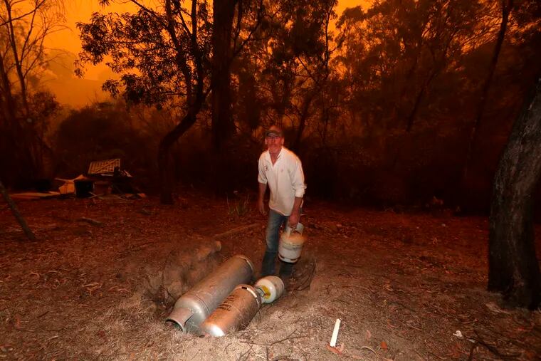 Evan Harris places gas bottles in a hole as he rushes around his property preparing to minimize fire impact at Burragate, Australia, Friday, Jan. 10, 2020, as a nearby fire threatens the area. Thousands of people are fleeing their homes and helicopters are dropping supplies to towns at risk of wildfires as hot, windy conditions threaten already fire-ravaged southeastern Australian communities.