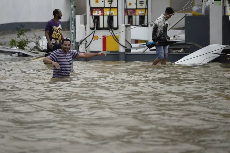 People walk next to a gas station flooded and damaged by the impact of Hurricane Maria.