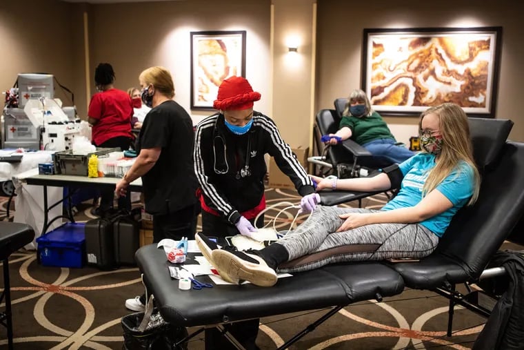 Blood donor Emily Henman (far right) watches as Red Cross nurse Rickeya Alton prepares to start her blood donation during a Red Cross Blood Drive at the Embassy Suites in St. Charles, Mo., on Feb. 8, 2021. With typical locations like schools and corporate offices less available because of the pandemic, the Red Cross has pivoted to holding blood drives in less typical locations, like hotels.