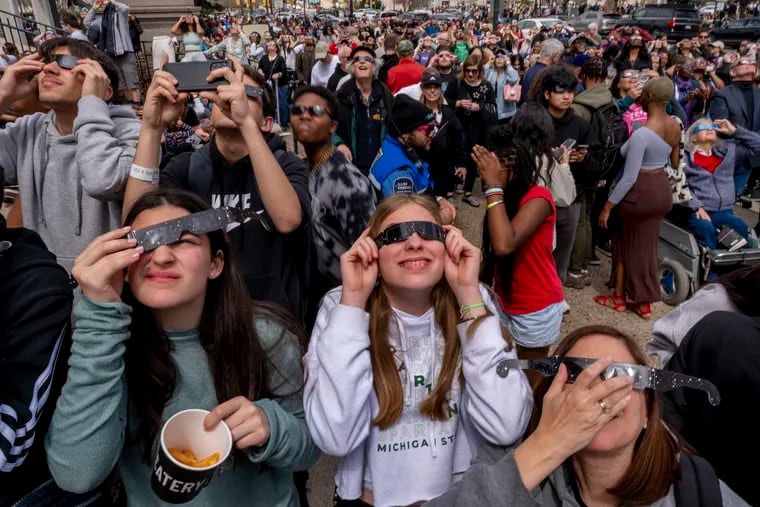 People react as the clouds lift and they get their first look at the partial eclipse during a free community-wide eclipse viewing party at the Franklin Institute.
