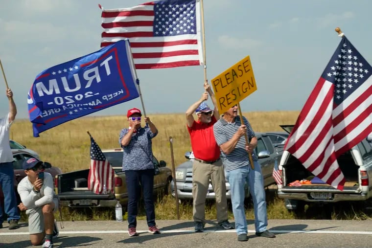 Protesters hold signs on the side of the road as seen through the window of a motorcade vehicle traveling with President Joe Biden to the Flatirons Campus of the National Renewable Energy Laboratory, on Sept. 14, 2021, in Arvanda, Colo.