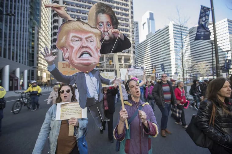 Carla Krash, center, operates a puppet of President Trump with Steve Bannon holding the strings as she and the other protesters march around City Hall on Monday afternoon.  There was a rally at the Thomas Paine Plaza on Presidents&#039; Day to protest the Trump administration&#039;s executive orders.