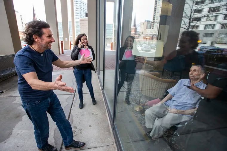 Rich Landau (left) greets his father Mike Landau (right) with his sister Suzanne Landau during a window visit at The Watermark at Logan Square, a retirement community. They are not allowed inside due to the virus and had not seen him for over a week.