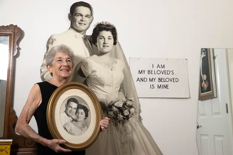 Dene Bloom holding a photo next to a large cutout of her and her late husband, Marvin Bloom, on their wedding day.